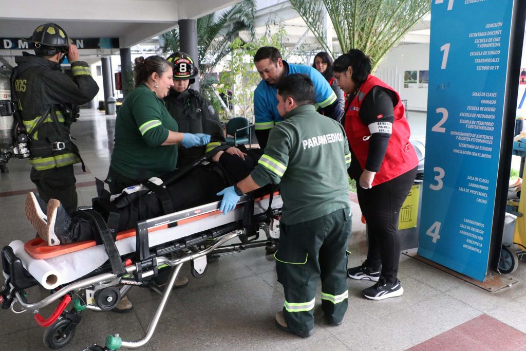 Paramédicos de la ACHS y bomberos de la octava compañía de Peñalolén, realizan procedimientos a persona lesionada en el contexto de un simulacro en el Instituto Profesional ARCOS