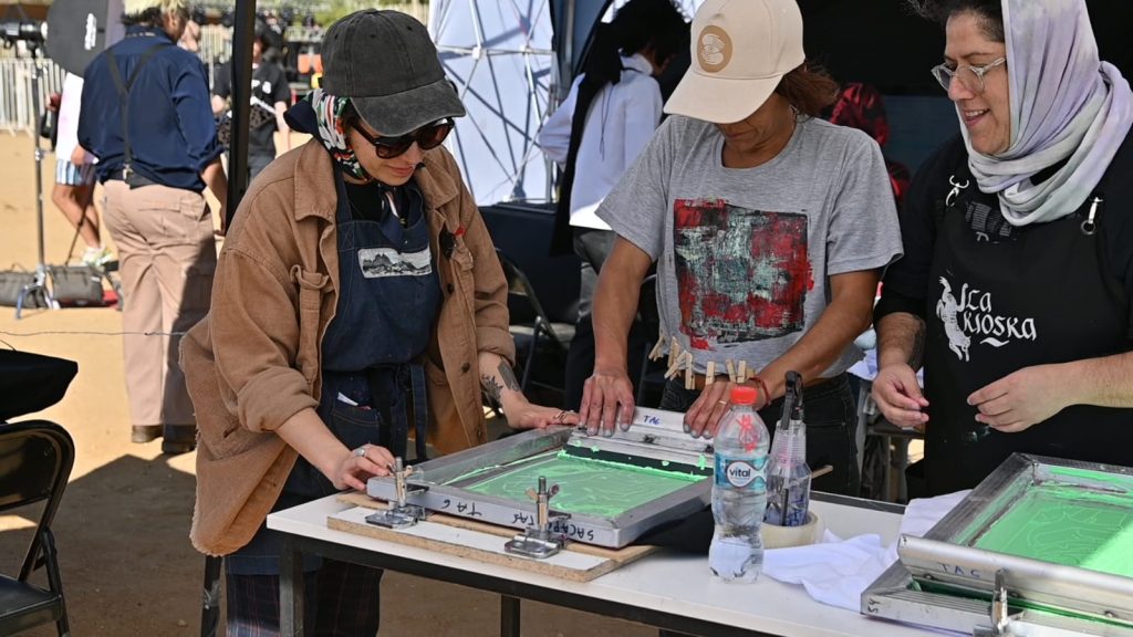 La Escuela de DIseño y Multimedia hace impresiones de serigrafía sobre artistas de Festival Rockódromo 2023 en el stand de I.P. ARCOS en el festival